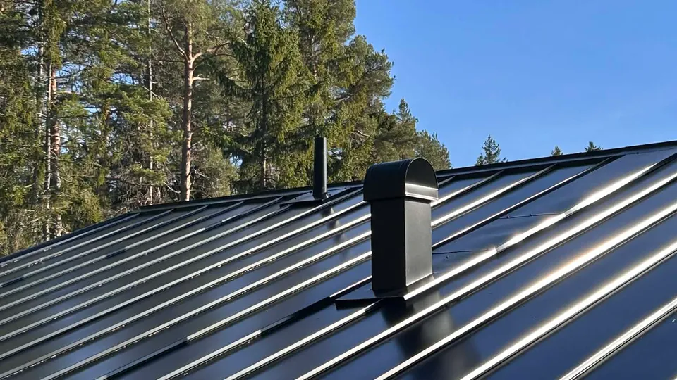 Närbild på nytt svart klicktak i plåt med skorstenshuv mot blå himmel