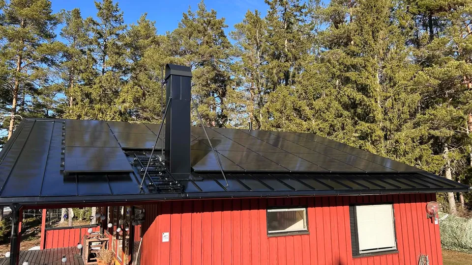 Solpaneler monterade på nytt svart plåttak på ett rött hus i Roslagen
