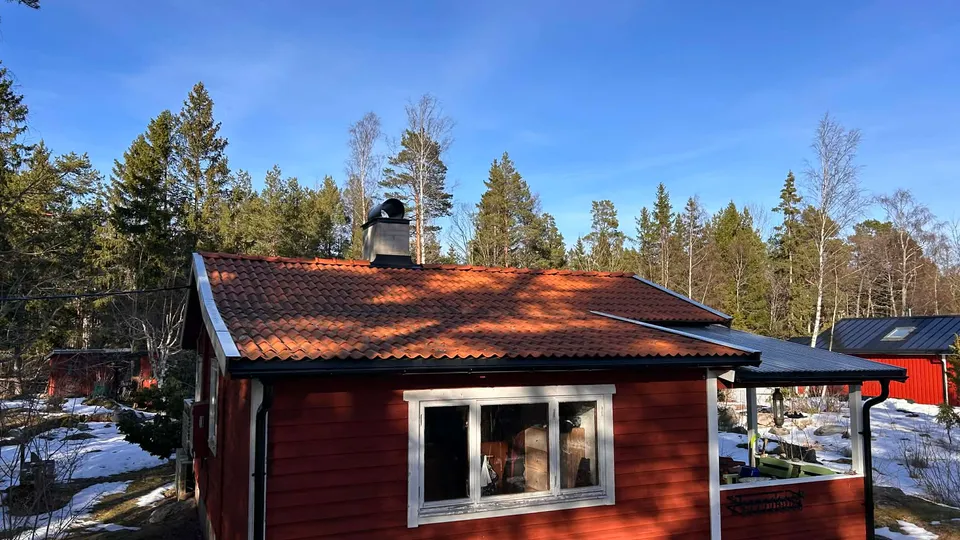 Nylagt rött tegeltak på ett rödmålat hus i vinterlandskap i Roslagen